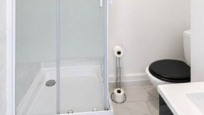 A modern bathroom with a glass-enclosed shower, a toilet, and a sink. - Studio cosy climatisé - Parking gratuit inclus (Le Bourget)