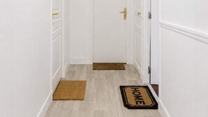 A hallway with white walls, a wooden floor, a door with a 'GLORY' sign, and a doormat with 'HOME' on it. - Studio cosy climatisé - Parking gratuit inclus (Le Bourget)