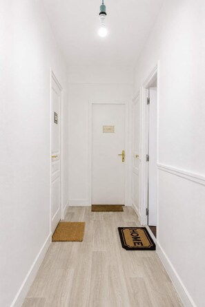 Ein Flur mit weißen Wänden, Holzboden, einer Tür mit dem Schild 'GLORY' und einer Fußmatte mit der Aufschrift 'HOME'.