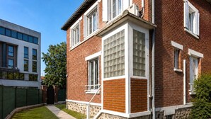 A two-story brick building with a stone base, large windows, and a visible staircase. - Studio cosy climatisé - Parking gratuit inclus (Le Bourget)