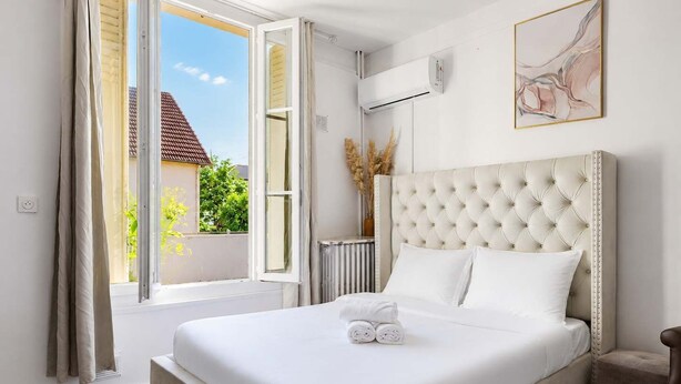 A hotel room with a large bed, a radiator, a window with curtains, and a wall-mounted air conditioner. - Studio cosy climatisé - Parking gratuit inclus (Le Bourget)