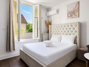 A hotel room with a large bed, a radiator, a window with curtains, and a wall-mounted air conditioner. - Studio cosy climatisé - Parking gratuit inclus (Le Bourget)