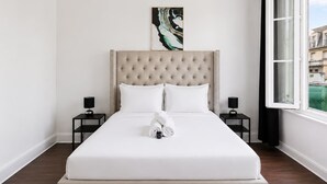 A hotel room with a large bed, two bedside tables, a headboard, and a window with a view of buildings. - Appartement lumineux climatisé - Parking (Le Bourget)