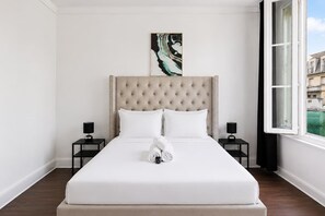 Ein Hotelzimmer mit einem großen Bett, zwei Nachttischen, einer Kopfteil und einem Fenster mit Blick auf Gebäude.