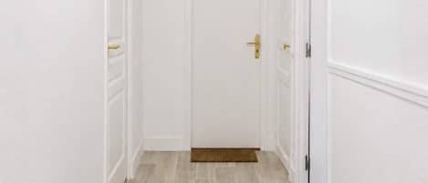A hallway with white walls, a wooden floor, a door with a 'GLORY' sign, and a doormat with 'HOME' on it.