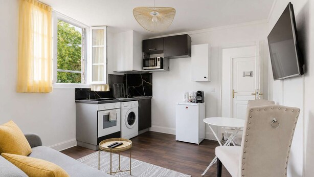 A compact living space with a kitchenette, a sofa, a dining table, and a television. - Appartement lumineux climatisé - Parking (Le Bourget)