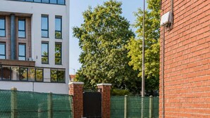 A pathway leading to a building with a brick facade and a green fence. - Appartement lumineux climatisé - Parking (Le Bourget)