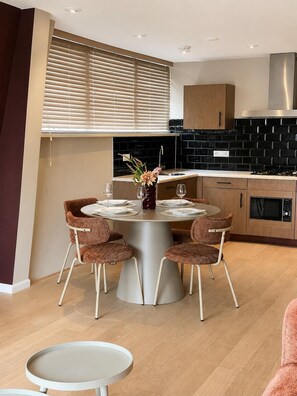 A modern kitchen with black tiled backsplash, wooden cabinets, and a round dining table with four chairs.