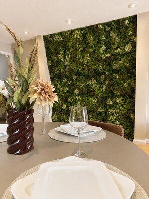 A dining table set with white plates, a clear wine glass, and a decorative vase with flowers.