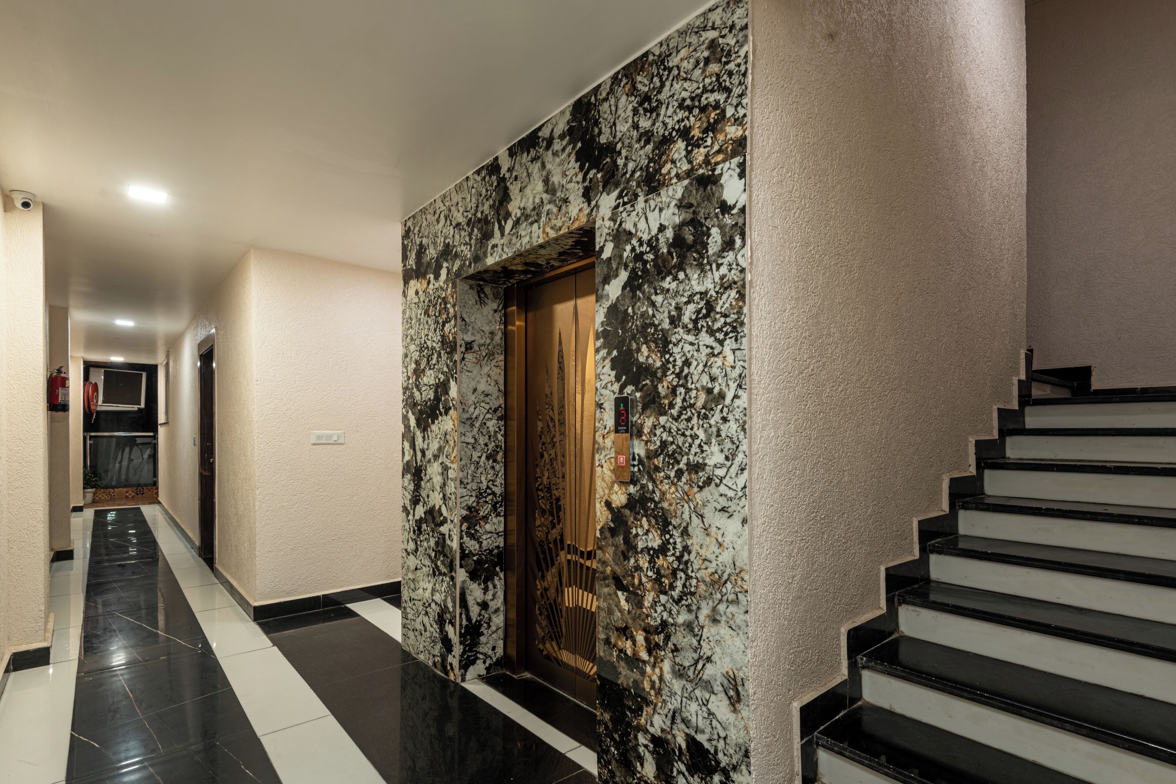A hallway with a marble wall, a wooden door, and a staircase.