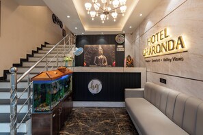 Un vestíbulo de hotel con una escalera, un mostrador de recepción, una estatua de Buda, un reloj y un letrero que dice 'HOTEL CHARONDA'.