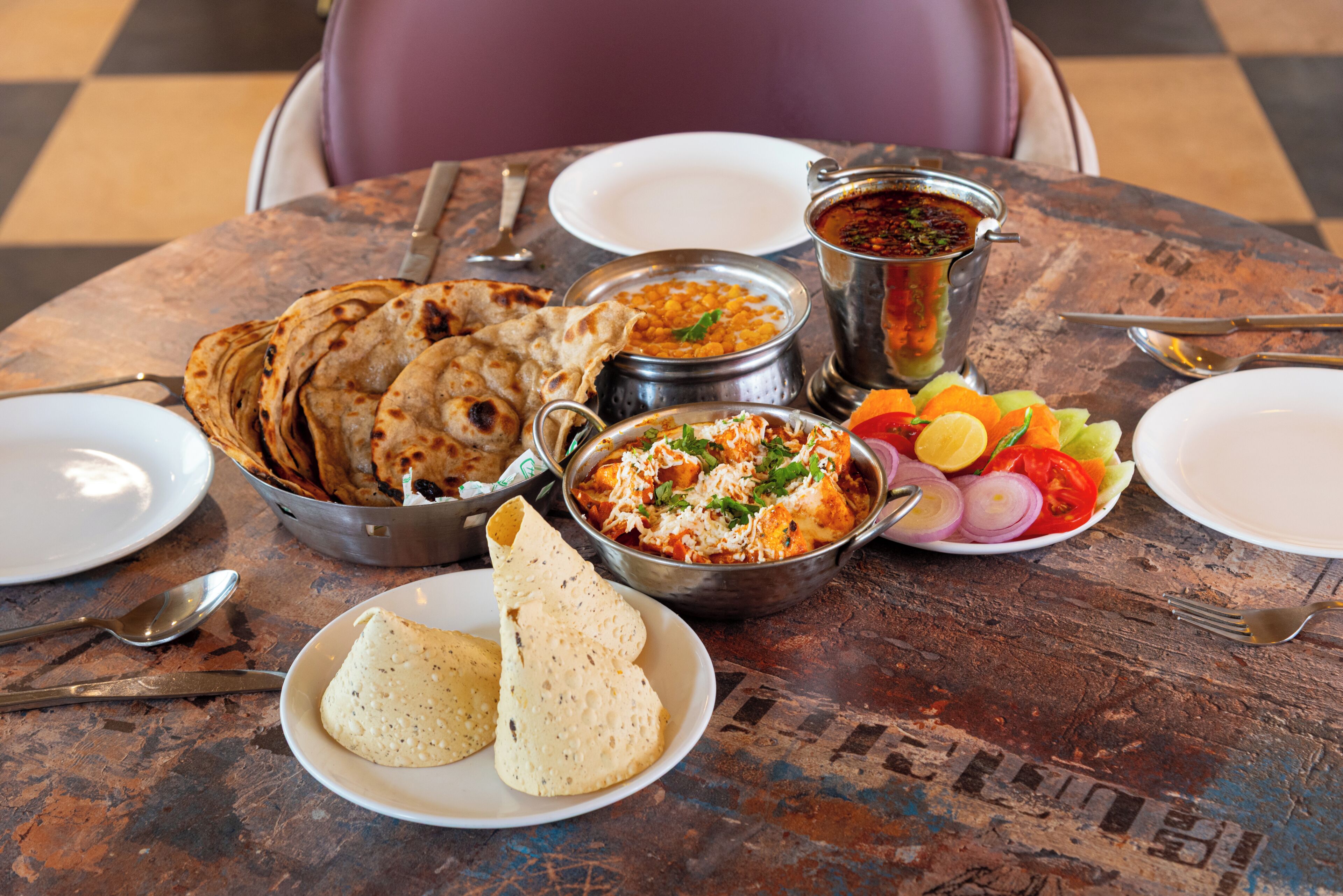 A table set with various Indian dishes, including naan bread, curry, and a salad.