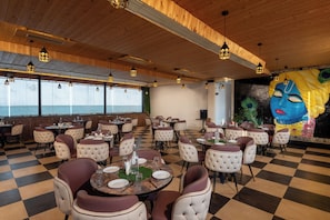 A restaurant with checkered flooring, round tables with chairs, pendant lighting, and a mural on the wall.