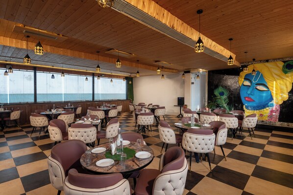 A restaurant with checkered flooring, round tables with chairs, pendant lighting, and a mural on the wall.