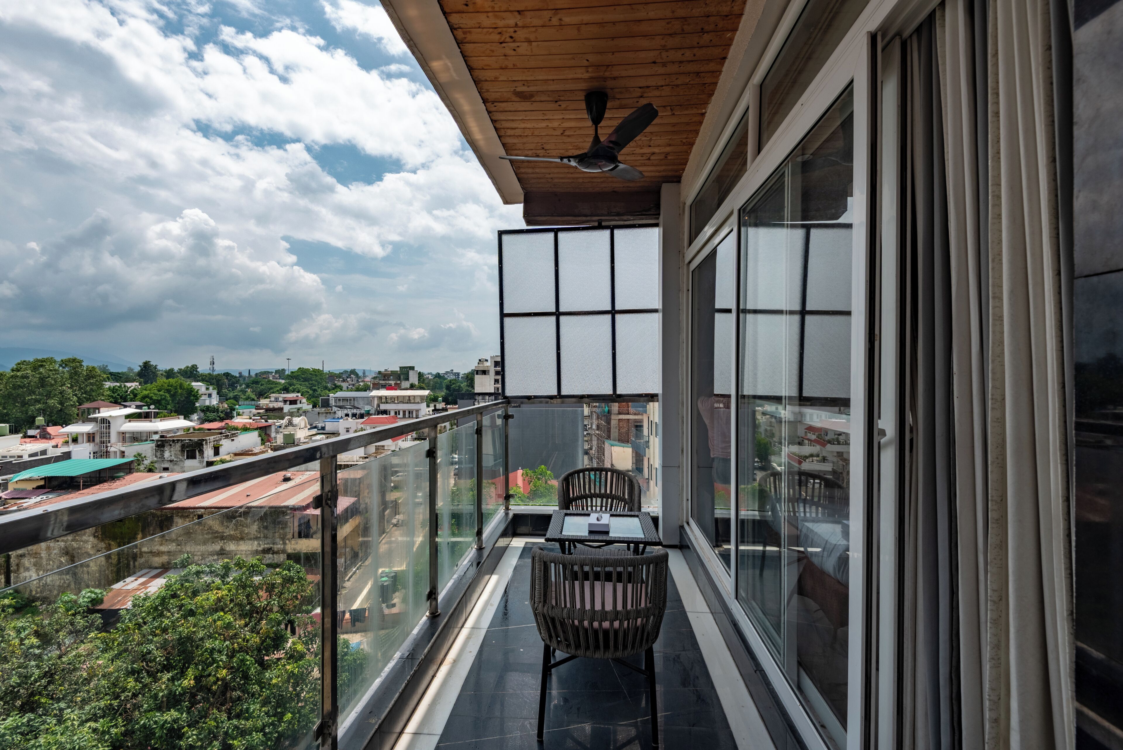 Un balcon avec une table et des chaises, un ventilateur de plafond et une vue sur le paysage urbain.