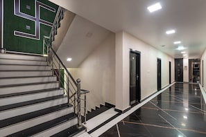 Pasillo de hotel con una escalera, puertas y un piso pulido.
