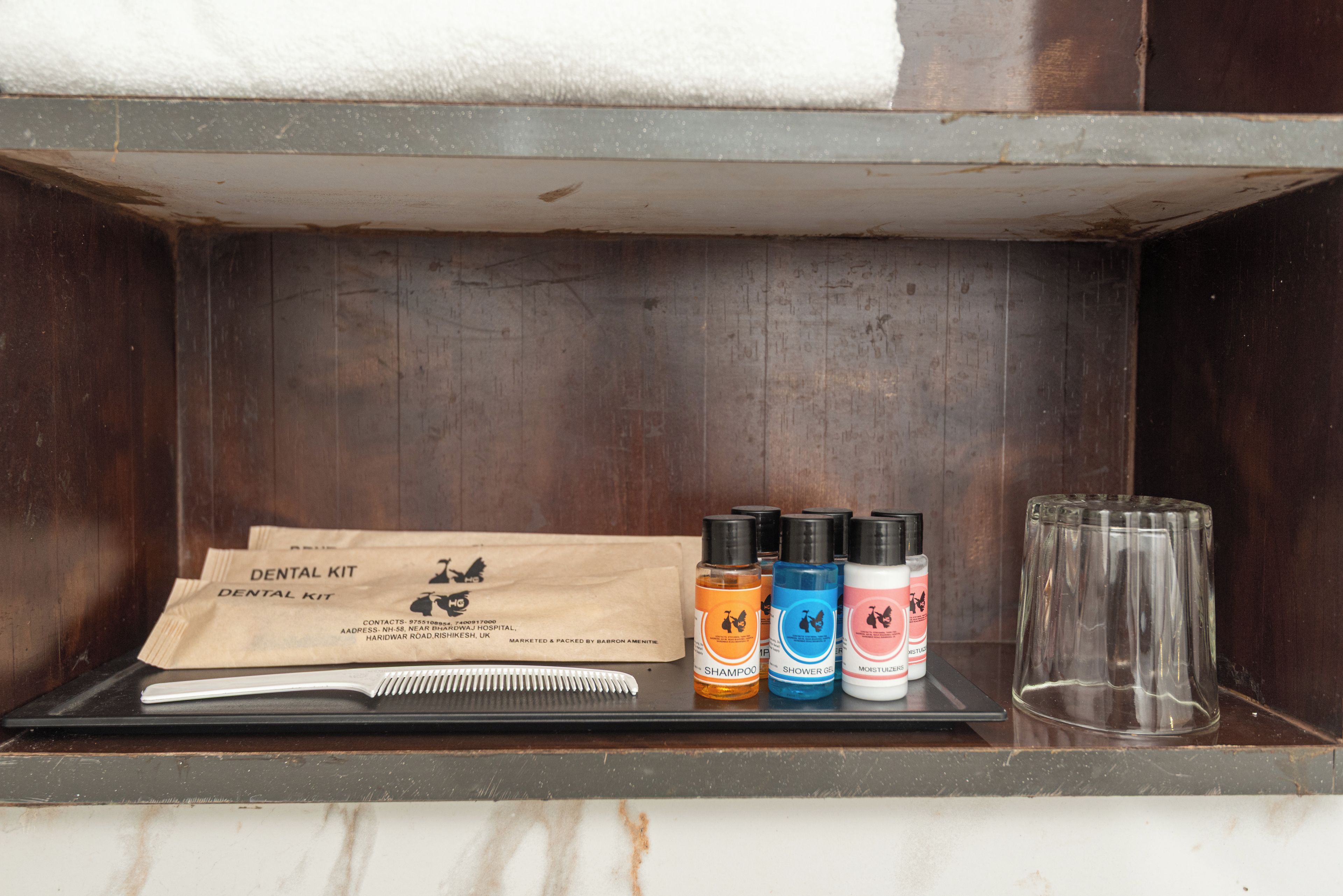 A wooden shelf with a dental kit, shampoo, shower gel, and a comb.