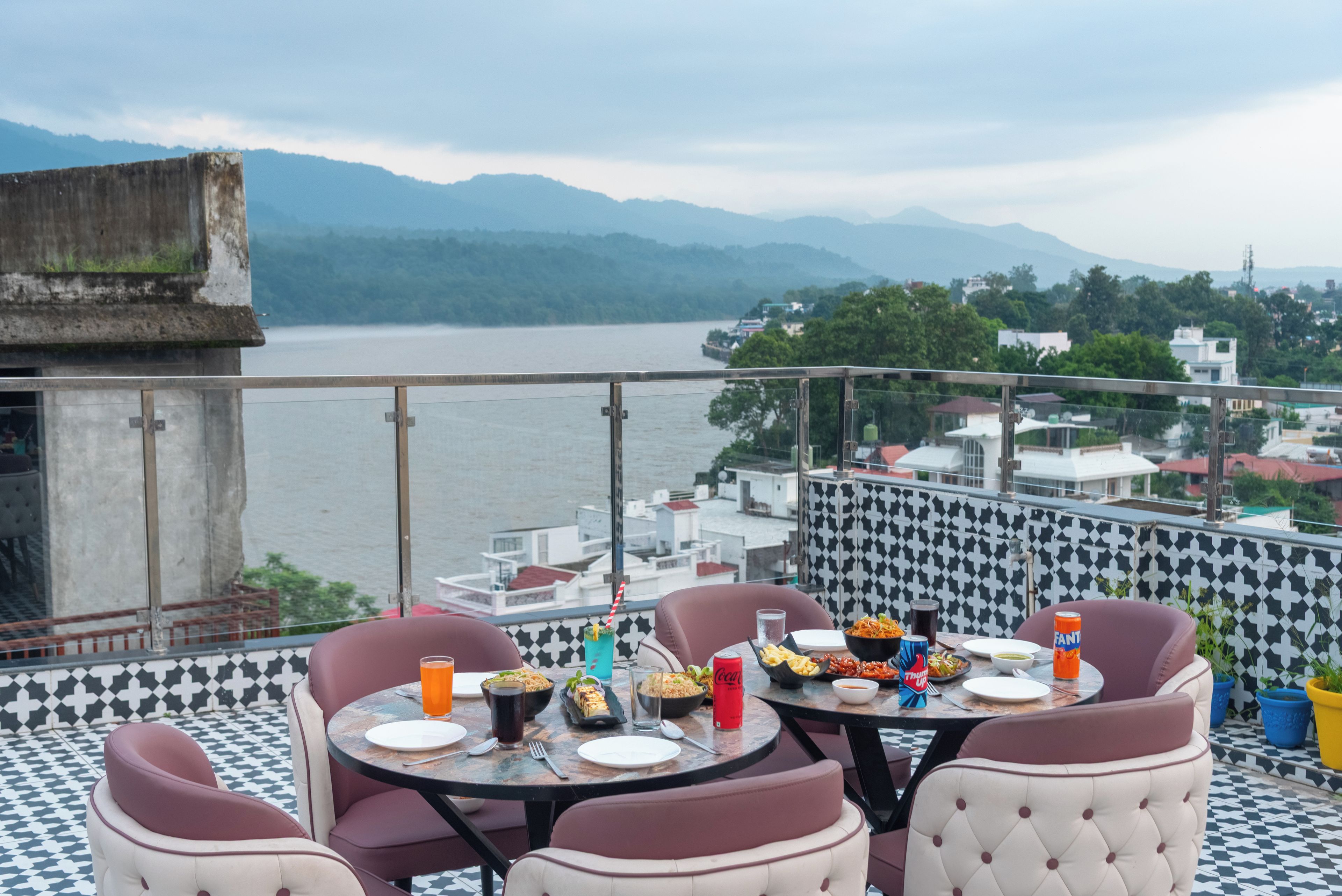 A terrace with round tables and chairs, a view of a lake, and a distant mountain range.