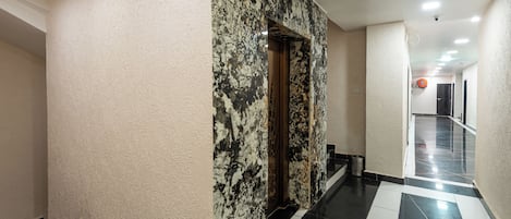 Un pasillo con pared de mármol y piso de baldosas blanco y negro.