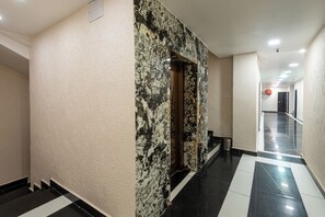 A hallway with a marble wall and a black and white tiled floor.