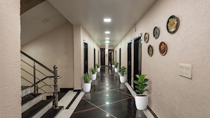 A hotel corridor with a staircase on the left, potted plants along the walls, and doors leading to rooms.