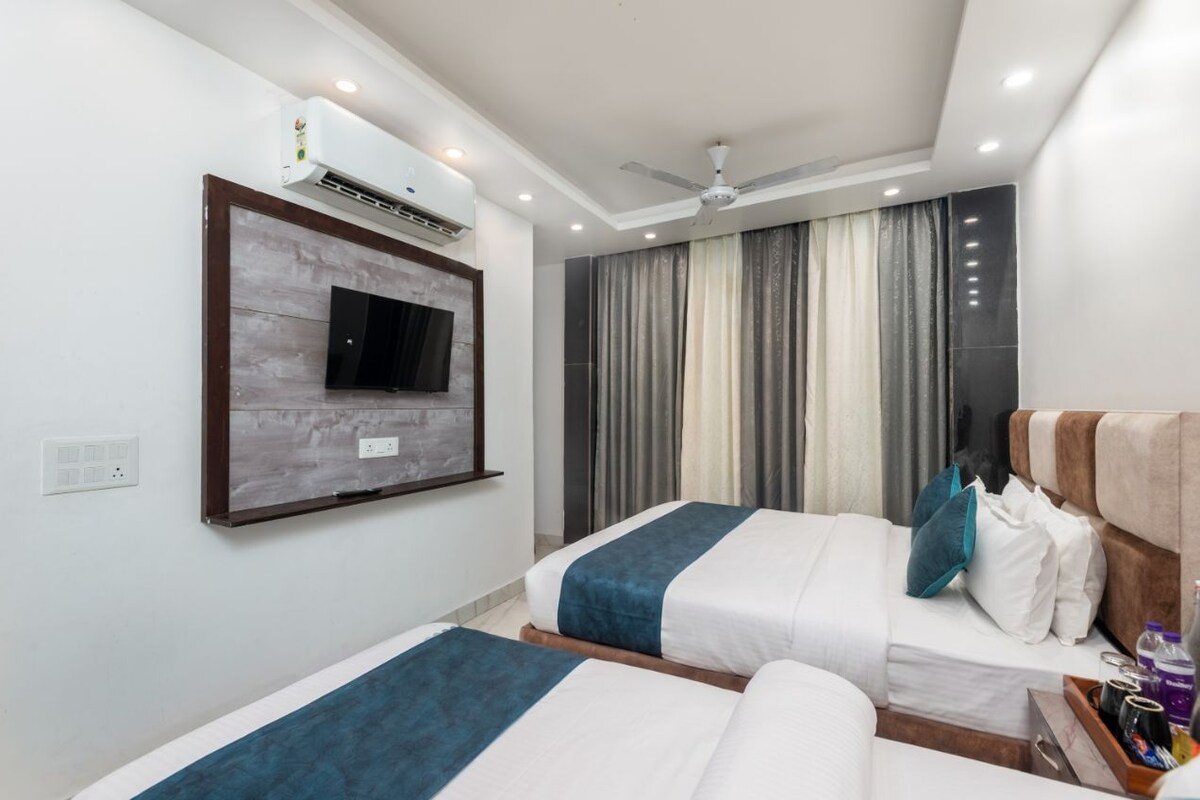 Habitación de hotel con dos camas, un televisor montado, unidad de aire acondicionado, ventilador de techo y ventana con cortinas.
