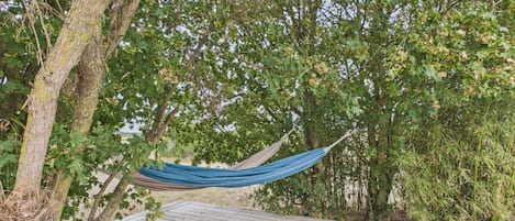 Eine Hängematte, die zwischen Bäumen auf einer Holzterrasse befestigt ist.