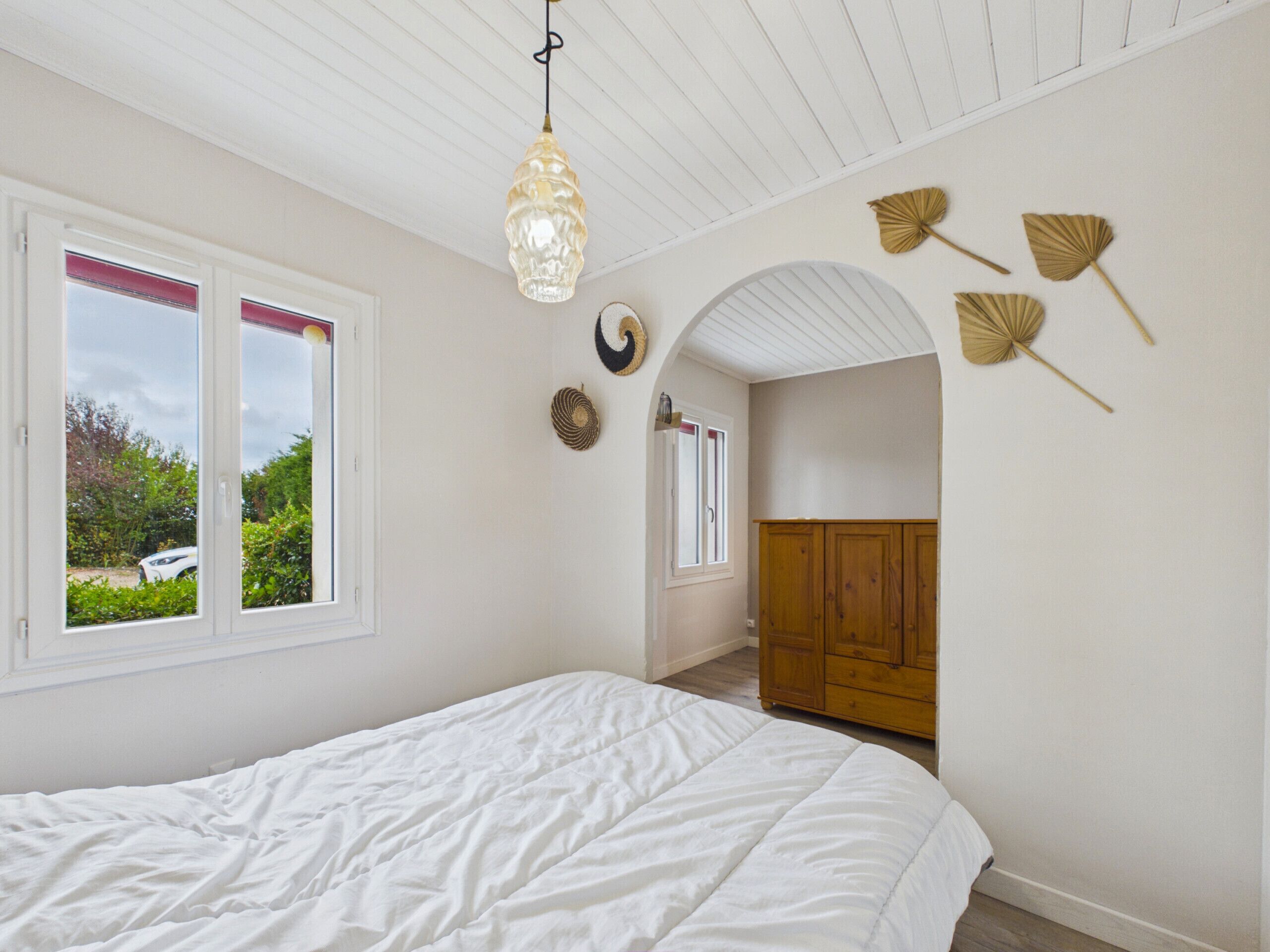 Um quarto com uma cama, uma janela e uma porta que dá para outro cômodo.
