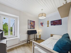 Ein Schlafzimmer mit Bett, Schreibtisch, Lampe und Fenster.