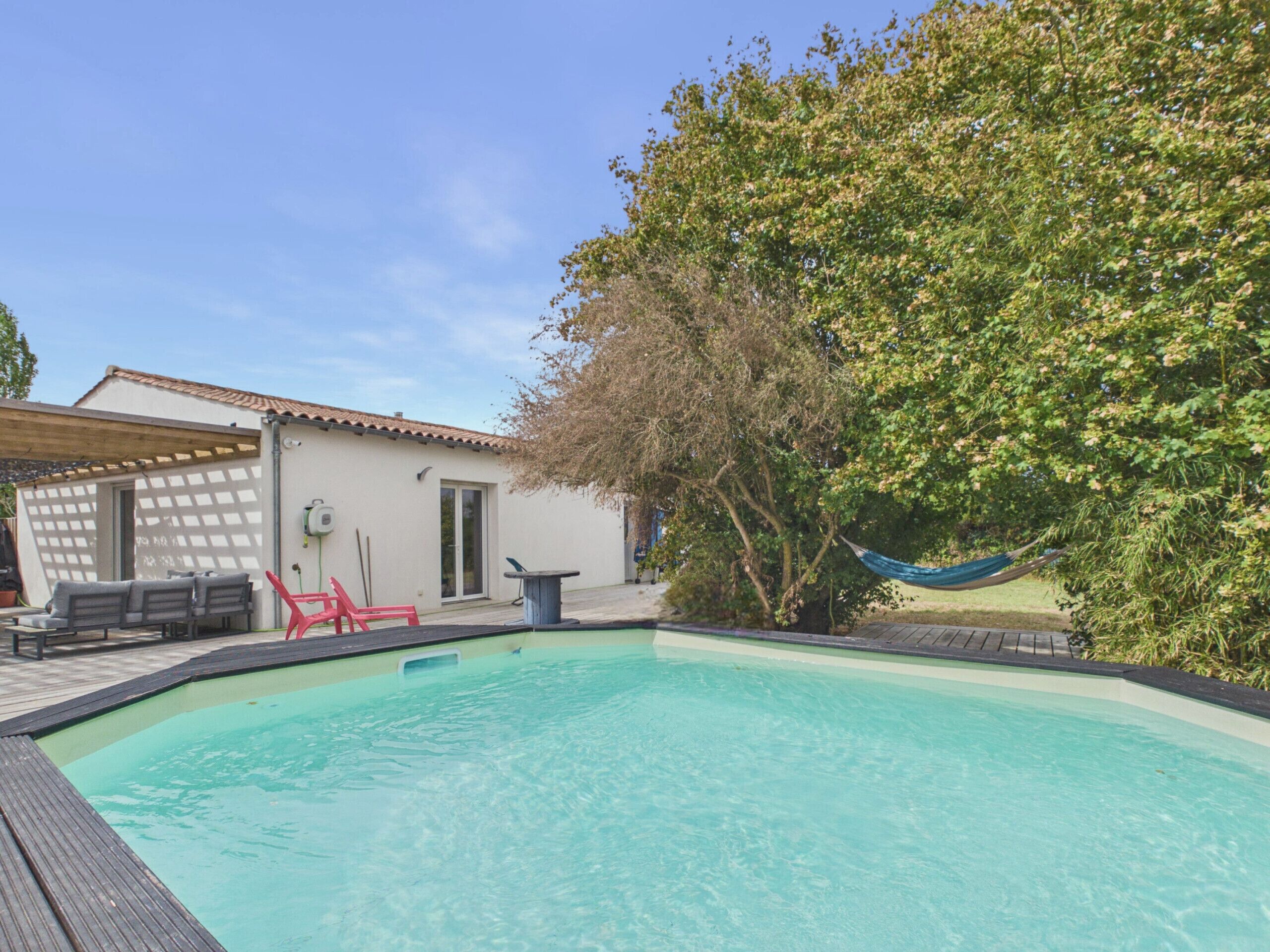 Ein Pool mit Holzterrasse, überdachter Sitzgelegenheit und einem Baum.
