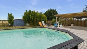 En swimmingpool med træterrasse, liggestole og et overdækket område med en Buddha-statue.