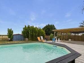 A swimming pool with a wooden deck, lounge chairs, and a covered area with a Buddha statue. - House with pool & large garden overlooking horses (Angles)