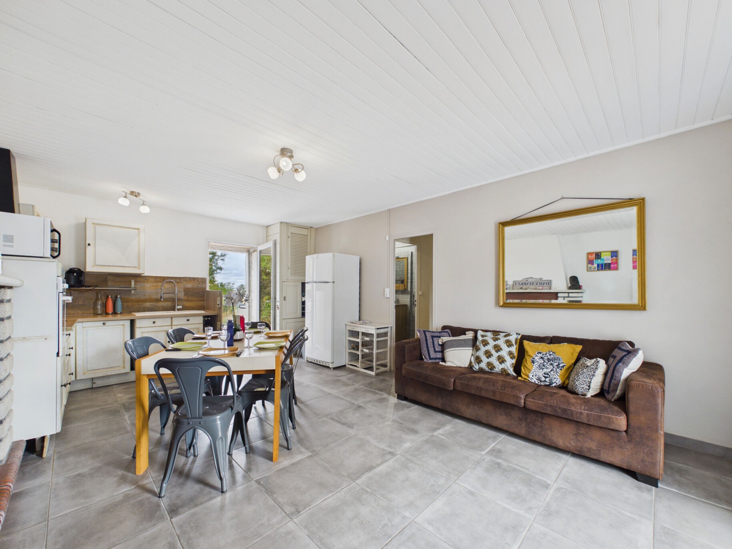 A modern kitchen with a dining area, a brown sofa with patterned cushions, and a large mirror on the wall.