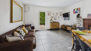 En stue med en lædersofa i brunt, et træskab, et spisebord med stole og en pejs.