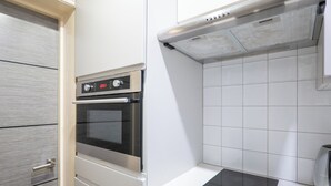 Una cocina con horno integrado, estufa y paredes de azulejos blancos.