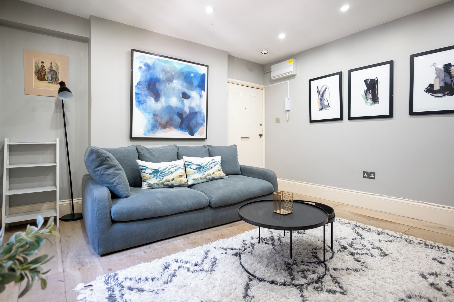 A modern living room with a grey sofa, abstract art, and a round coffee table.