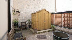 Un cobertizo de madera en un patio con un banco y plantas en macetas.