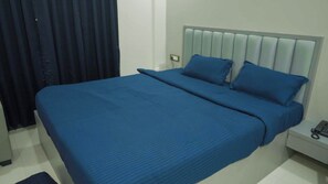 A bed with a headboard, a bedside table with a phone, and a window with curtains. - Rajdhani Premium Hotel (Bhubaneshwar)