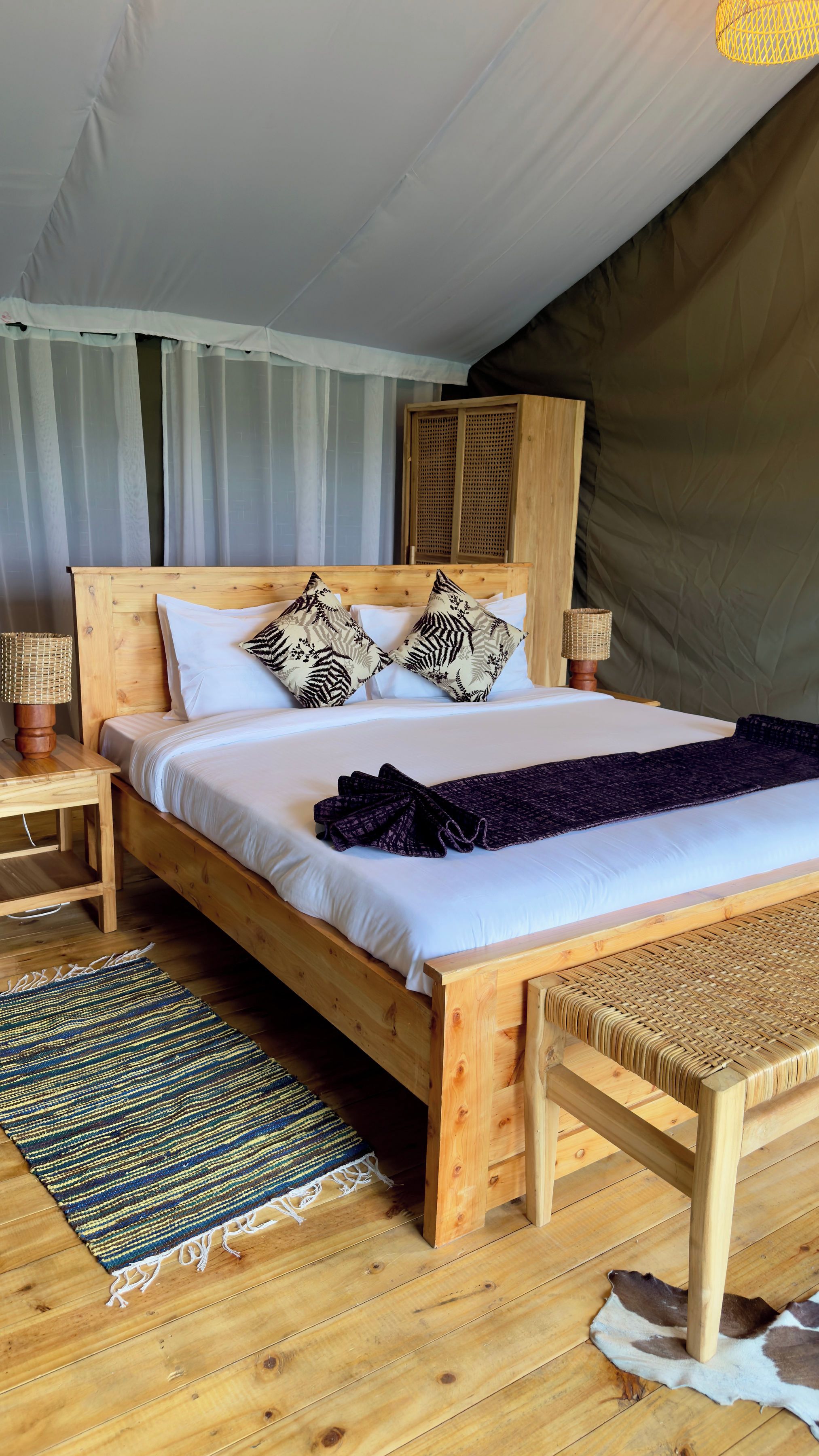 Uma cama de madeira com roupa de cama branca, um tapete tecido e um banco.