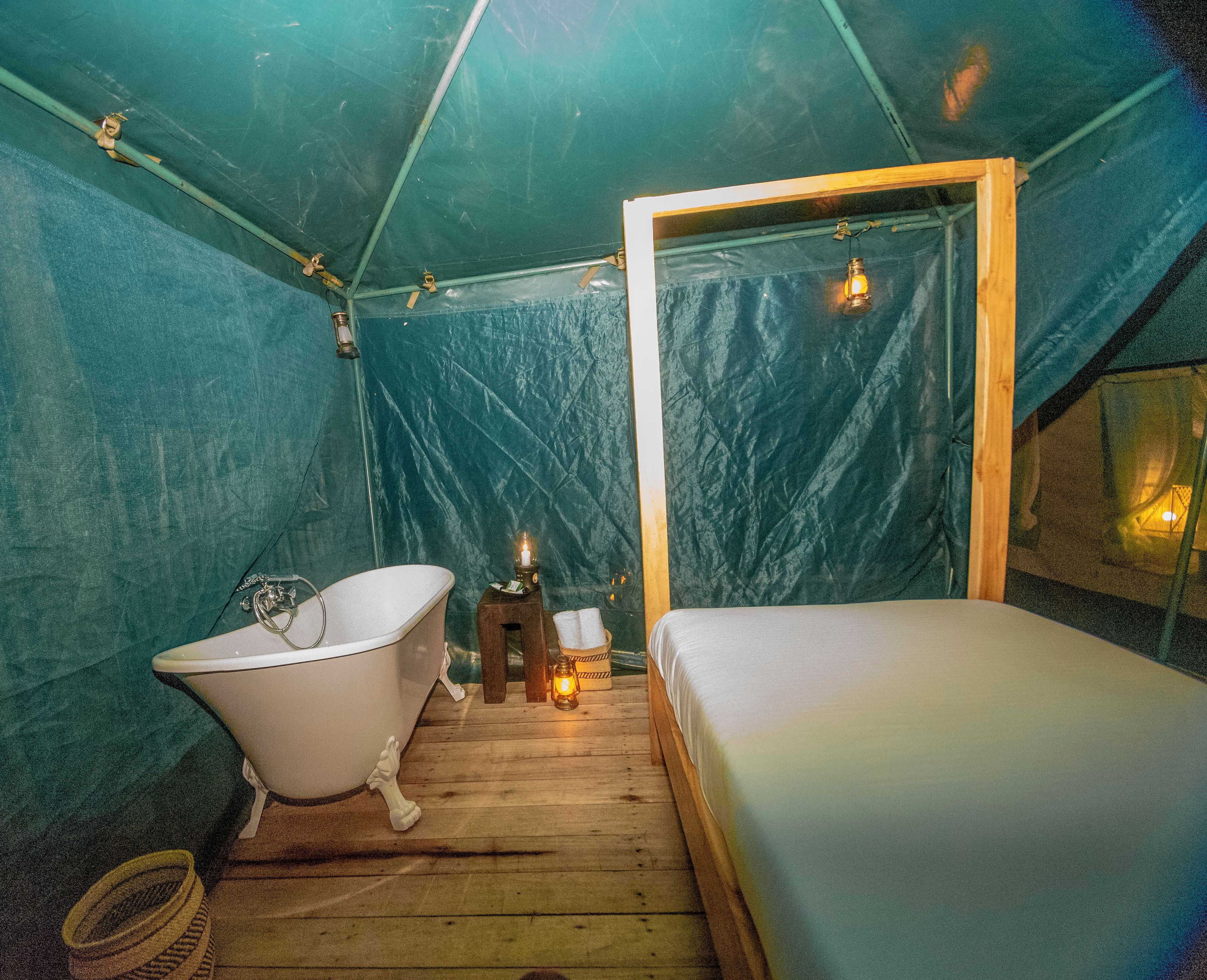 Una carpa con una cama individual, una bañera y una pequeña mesa con un farol.