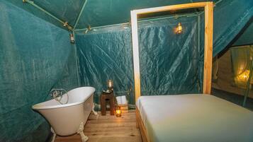 Una carpa con una cama individual, una bañera y una pequeña mesa con un farol.