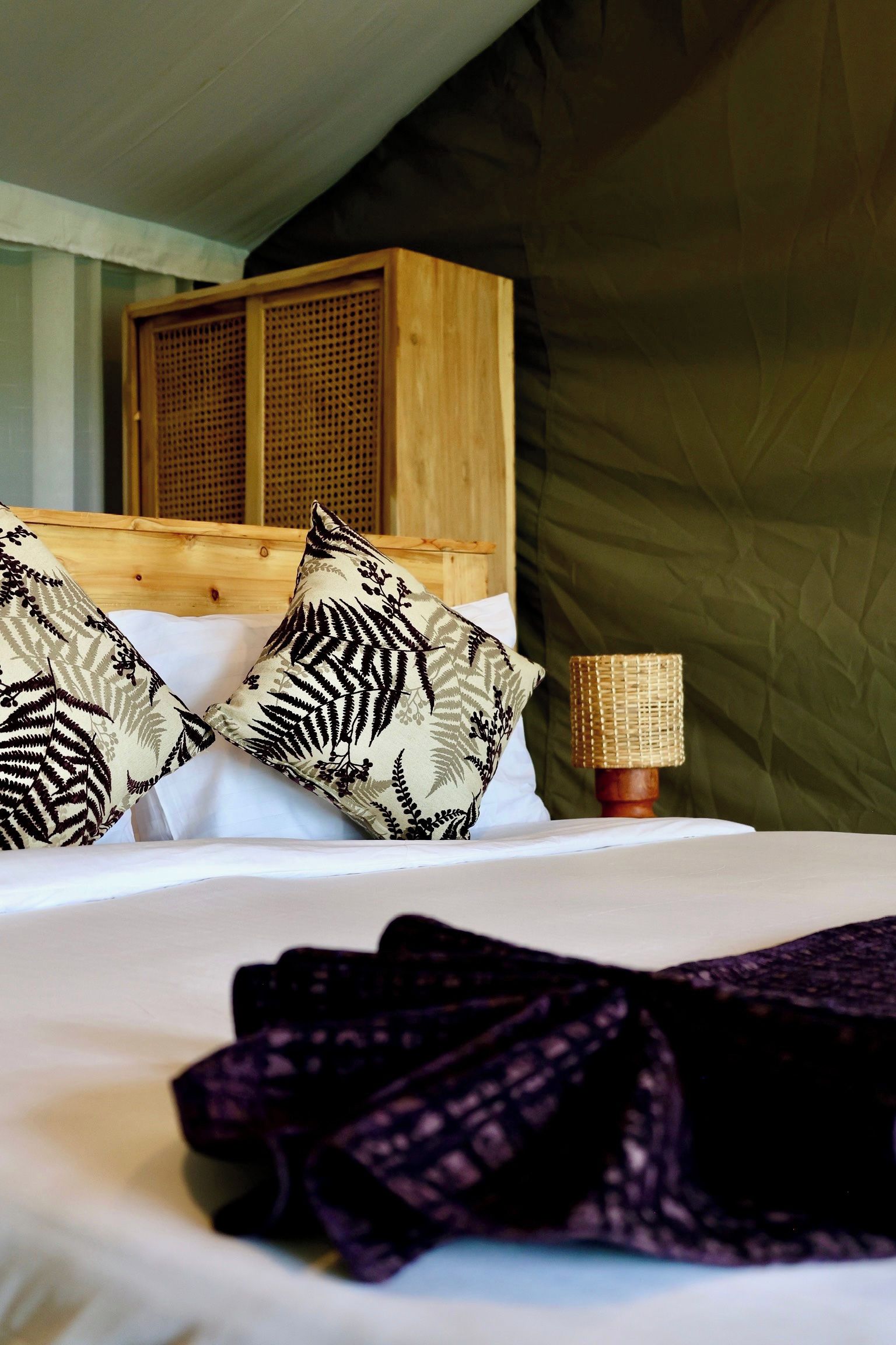A bed with two patterned pillows, a wooden headboard, and a woven lamp.