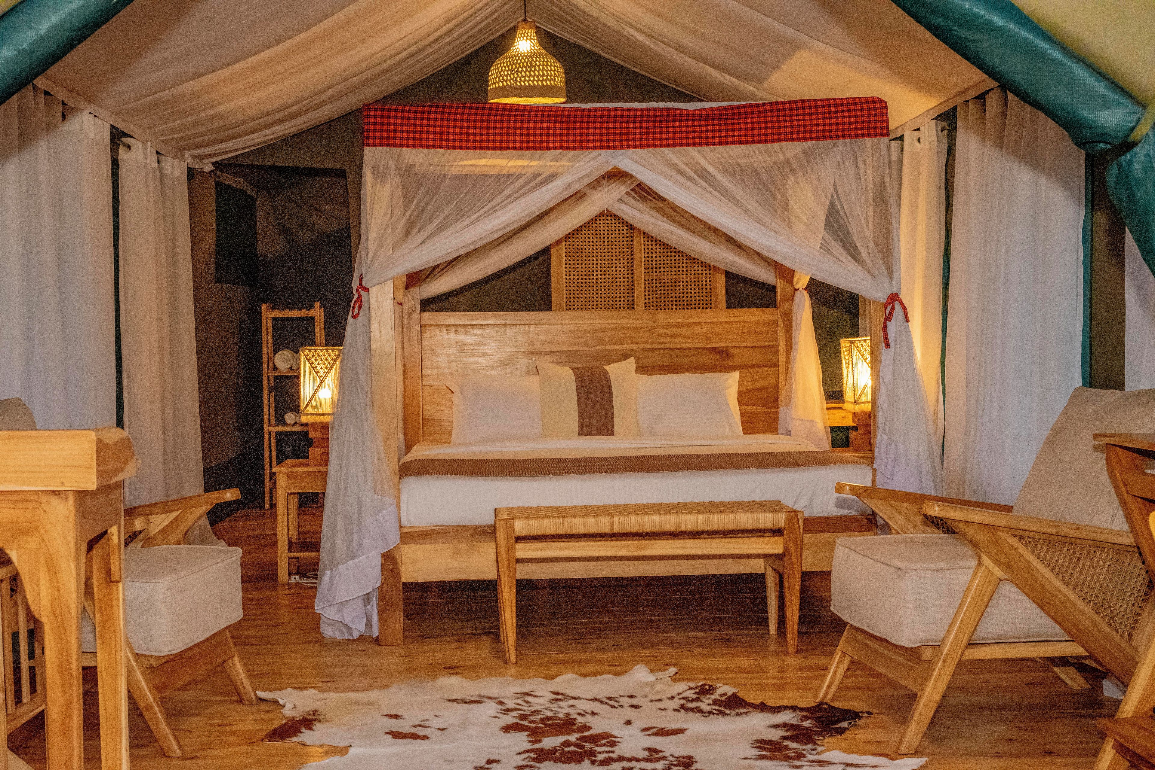 A cozy, well-lit tent-style room with a bed, two chairs, a bench, and a cowhide rug.