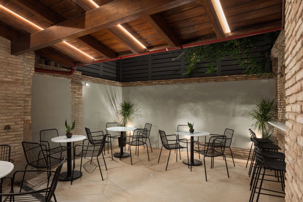 Un espace extérieur aménagé en terrasse, avec des tables et des chaises rondes, des murs en pierre et des poutres en bois.