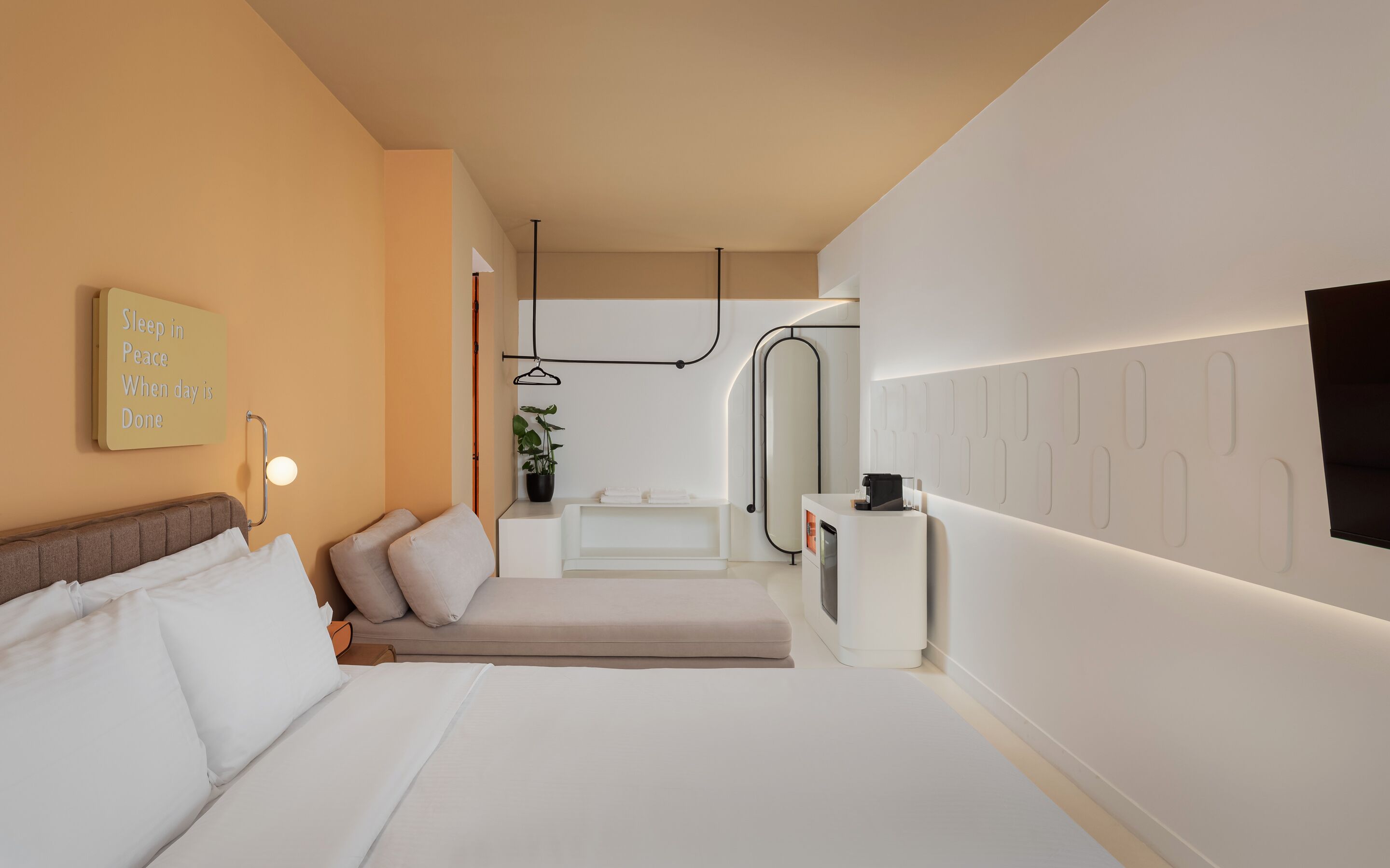 Habitación de hotel moderna con cama, mesita de noche, lámpara y una frase motivacional en la pared.