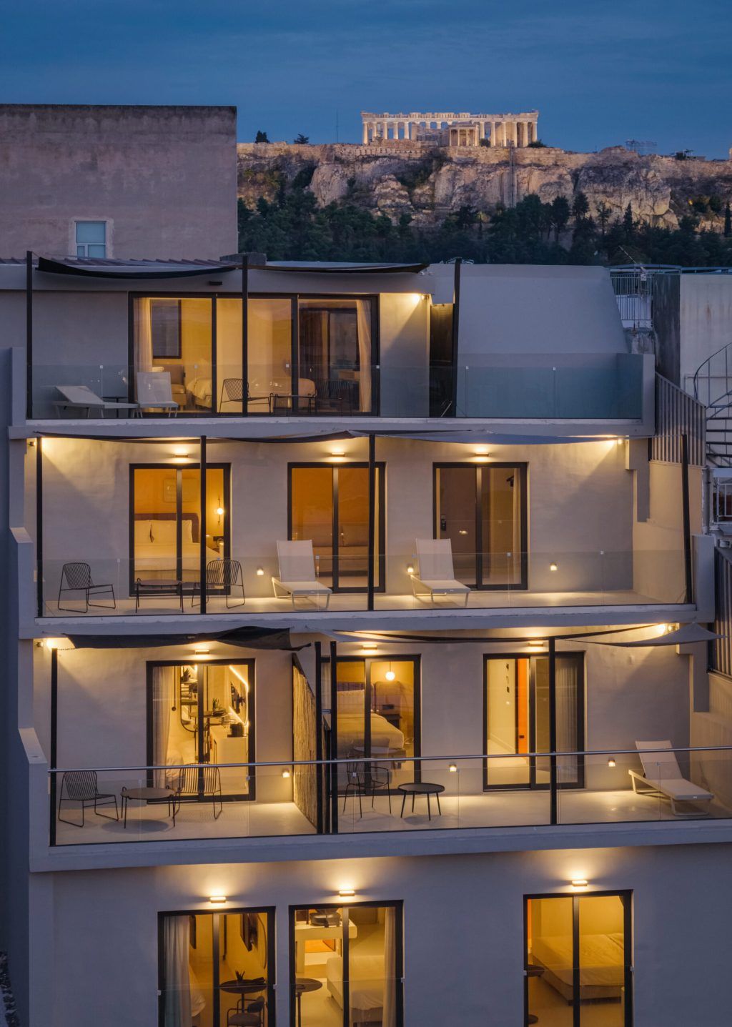 Un hotel a più piani con balconi, ampie finestre e vista sull'Acropoli sullo sfondo.