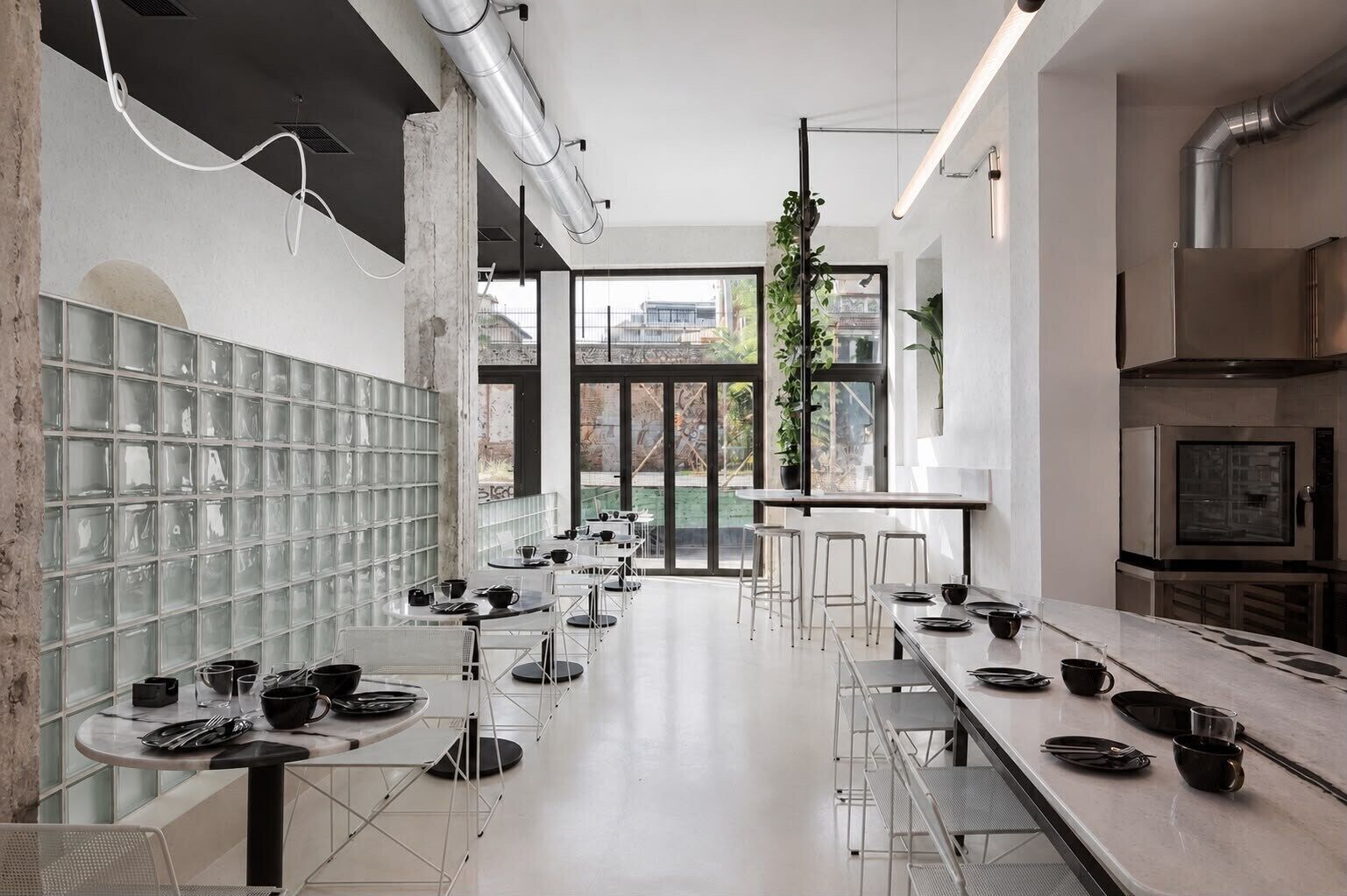 A modern kitchen with stainless steel appliances, a long dining table, and a glass block wall.