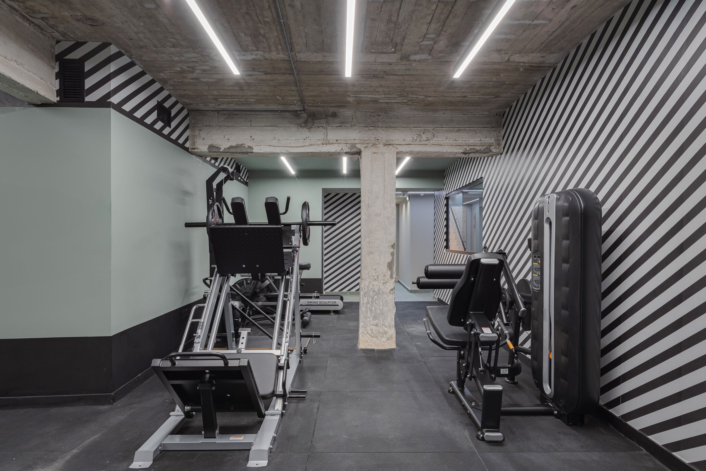 Ett gym med olika typer av träningsutrustning, inklusive löpband och styrketräningsmaskiner, belyst med lysrör.