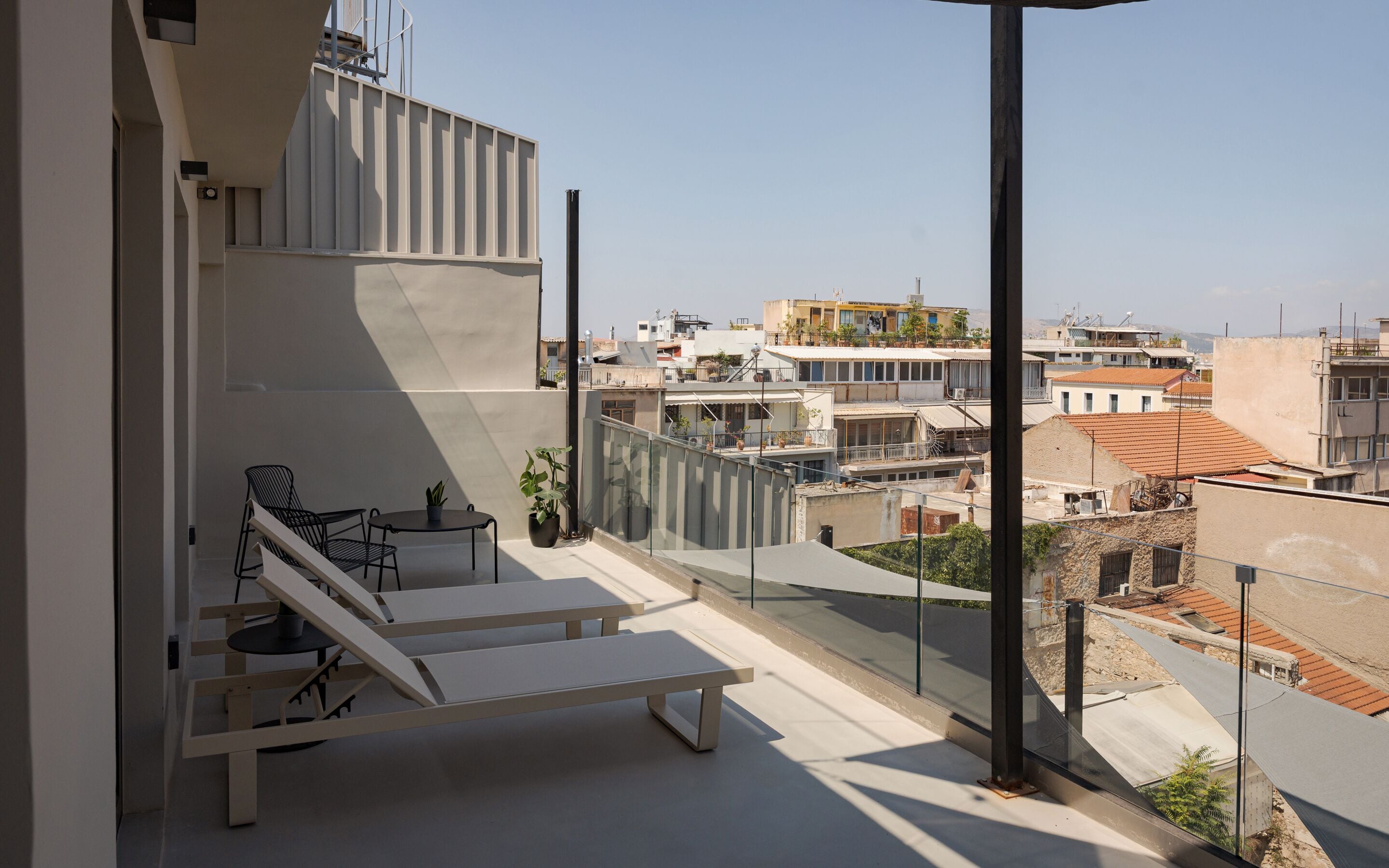 Een modern balkon met een minimalistisch design, voorzien van een lounge stoel, een klein tafeltje en potplanten.
