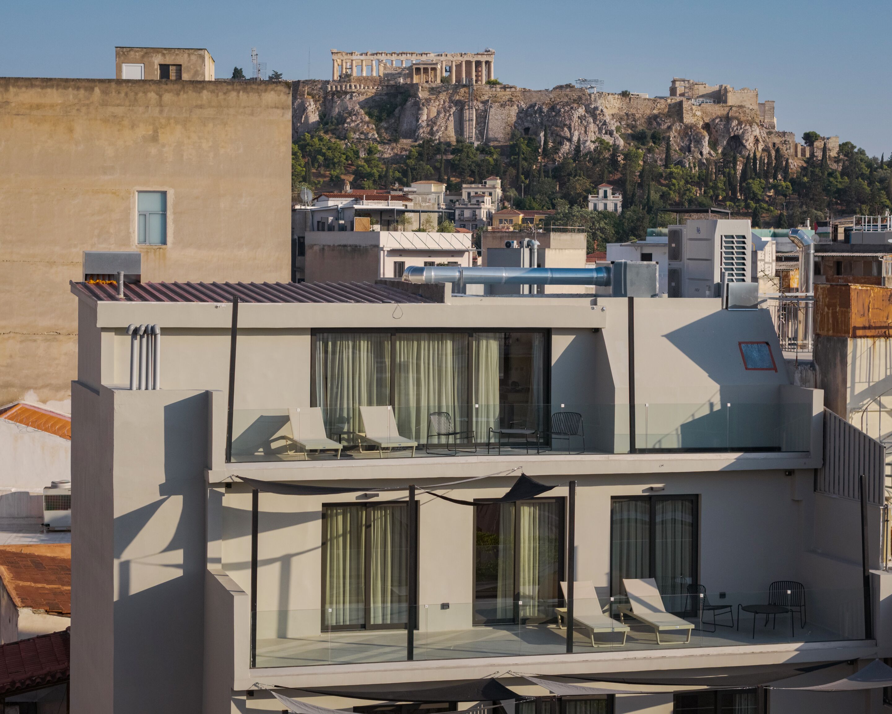 A modern building with a rooftop terrace featuring lounge chairs and a glass balustrade.